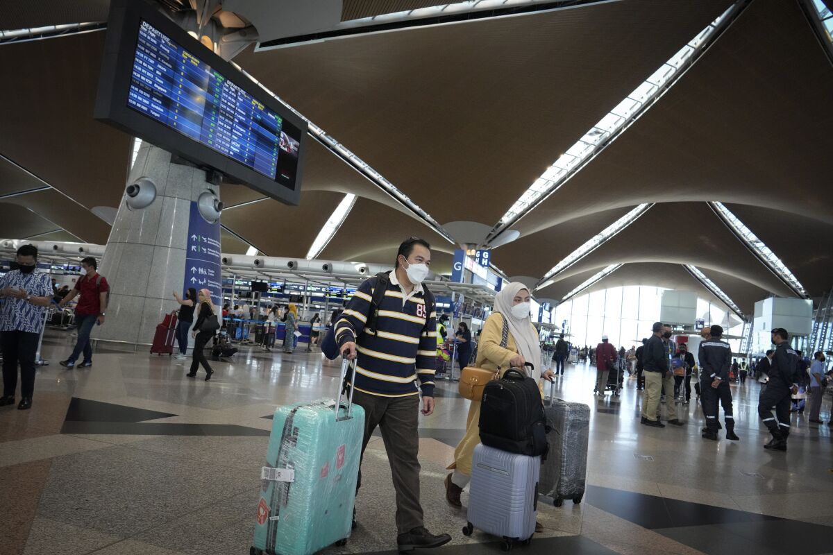 Travelers walk to check in counter at Kuala Lumpur International Airport in Sepang, Malaysia, Friday, April 1, 2022. Malaysia's international borders open to foreigners on Friday and fully vaccinated travelers do not have to undergo quarantine. (AP Photo/Vincent Thian)