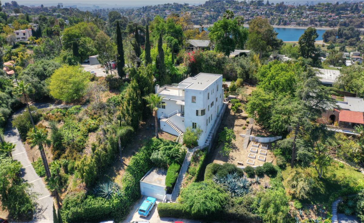 Aerial view of the three-story home surrounded by trees and bushes and other homes.