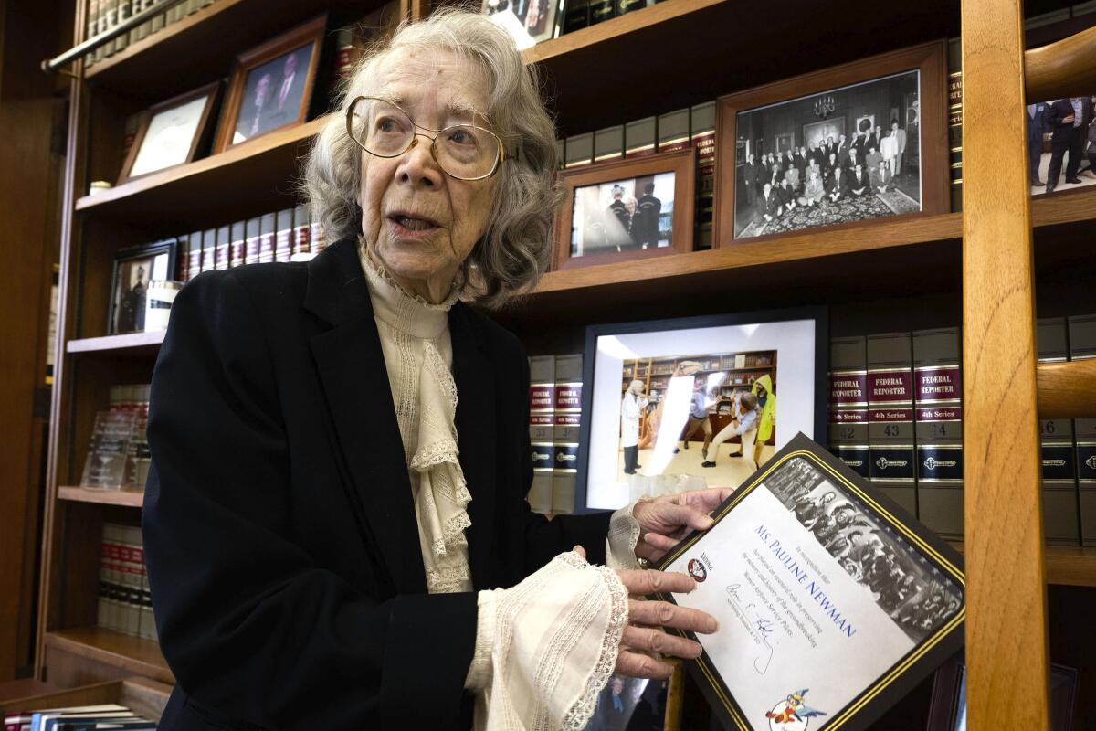 Federal appeals court Judge Pauline Newman stands next to a bookcase holding a certificate.
