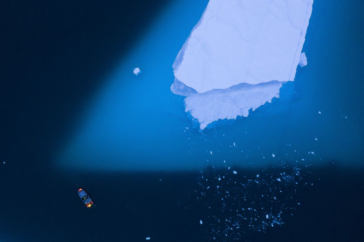 An aerial view of a boat next to a large iceberg in eastern Greenland.