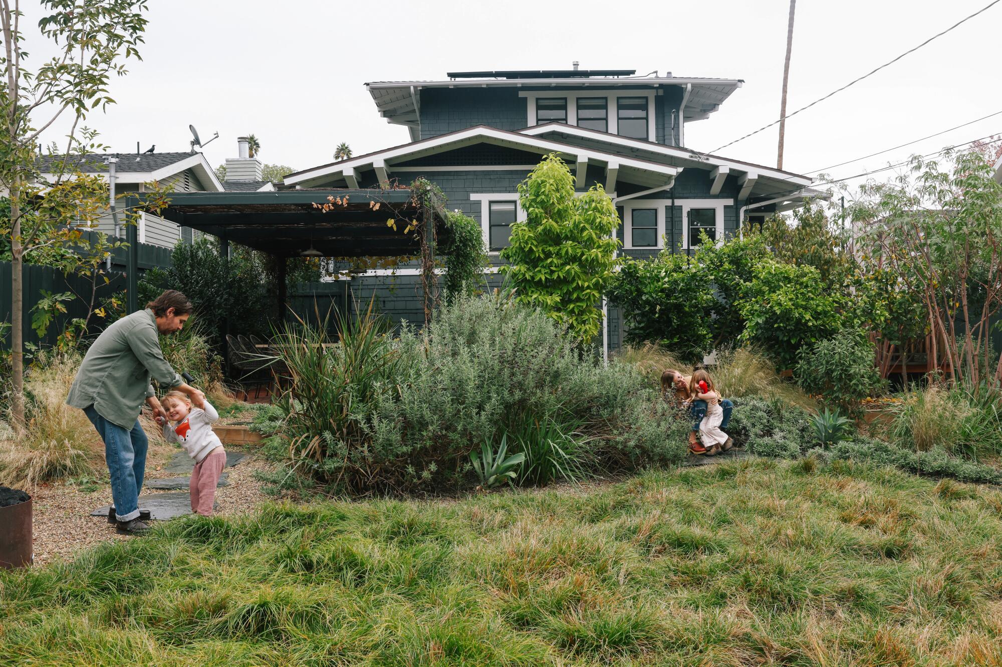 A mother and father and their two young daughters play in the backyard of their Craftsman-style house.