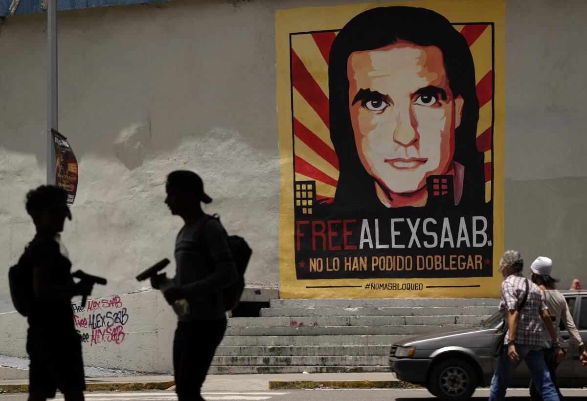 ARCHIVO - Peatones caminan cerca de un gran cartel del empresario colombiano Alex Saab en Caracas, 