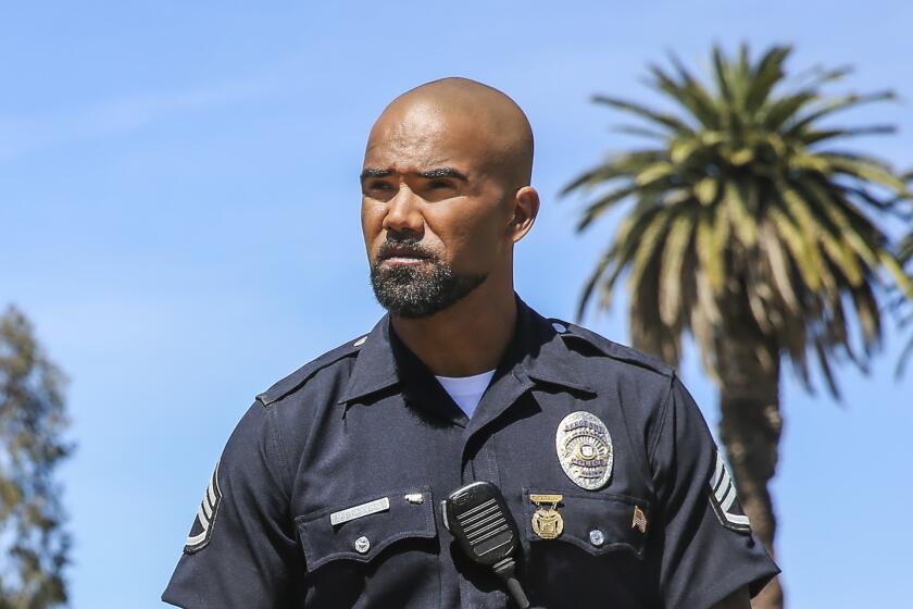 Shemar Moore walking in dark blue LAPD uniform on sunny day in front of palm trees and pedestrians