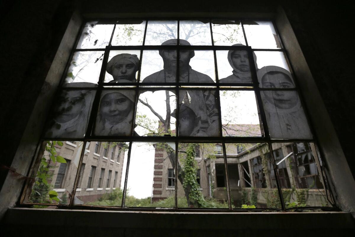 Images that are part of the exhibit "Unframed - Ellis Island" by artist JR are incorporated into a dilapidated window inside the contagious diseases ward of the Ellis Island hospital complex, Thursday, Sept. 25, 2014, in New York. The complex, which will be opened to the public for the first time ever on Oct. 1, 2014, stopped operating in 1954. In its day, the complex was the largest U.S. Public Health Service institution. Sick and pregnant immigrants were treated and cured before they were allowed to enter the country _ or were sent back to their native land. The facility included wards for contagious diseases, mental health and obstetrics. (AP Photo/Julio Cortez) ** Usable by LA and DC Only **