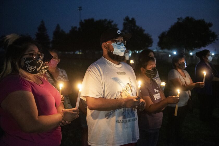 Foster Farms employee Kevin Vera, 28, of Livingston, center, attends a community candlelight vigil with family members at the Max Foster Sports Complex in Livingston, Calif., on Thursday, Sept. 3, 2020. The vigil was held to honor the eight lives lost and hundreds of families impacted by a COVID-19 outbreak at Foster Farms' Livingston plant.