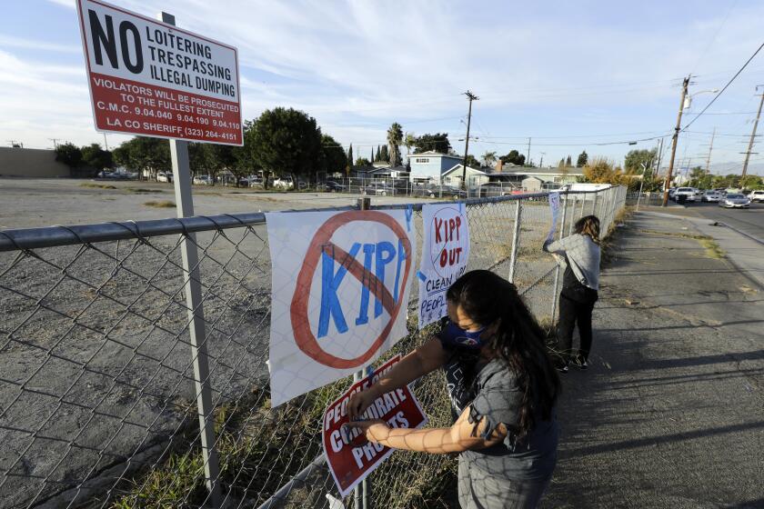 CUDAHY, CA - DECEMBER 09: Bertha Martinez, a teacher of 28 years in Cudahy, attaches a sign on the fence at a lot on Wednesday, Dec. 9, 2020 where the construction of a KIPP charter school is proposed. Community members spoke against the construction citing concerns about toxic soil, danger to people's health and increased traffic in the nieghborhood. (Myung J. Chun / Los Angeles Times)