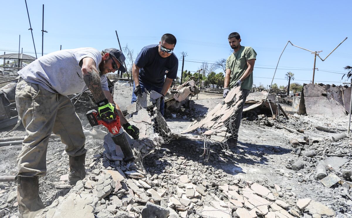 Two friends help Alvaro Baltierra, right, clear debris from his fire-ravaged home in Niland, Calif.