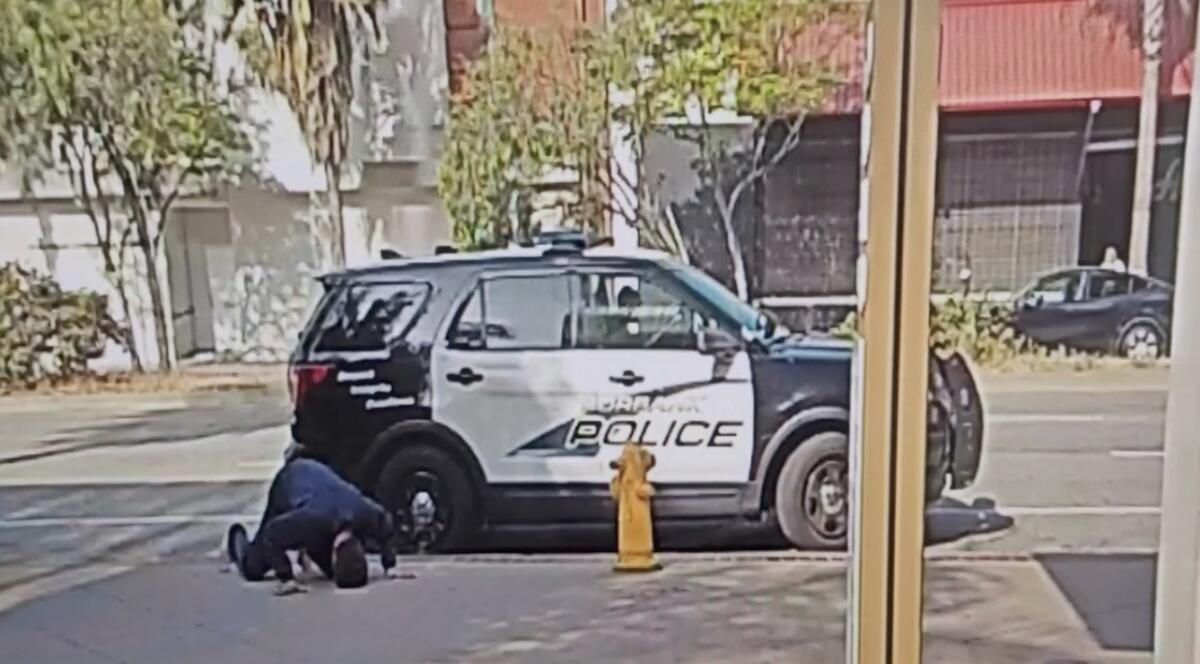 A man sprawling on the sidewalk next to a police vehicle.
