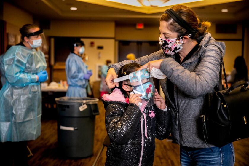 SAN DIEGO, CA - JANUARY 26: Brenda Alva helps her daughter Natalia Alva, 8, put her face shield back on after taking a COVID-19 test at a county testing center at San Diego State University's Parma Payne Goodall Alumni Center on Tuesday, Jan. 26, 2021 in San Diego, CA. (Sam Hodgson / The San Diego Union-Tribune)`