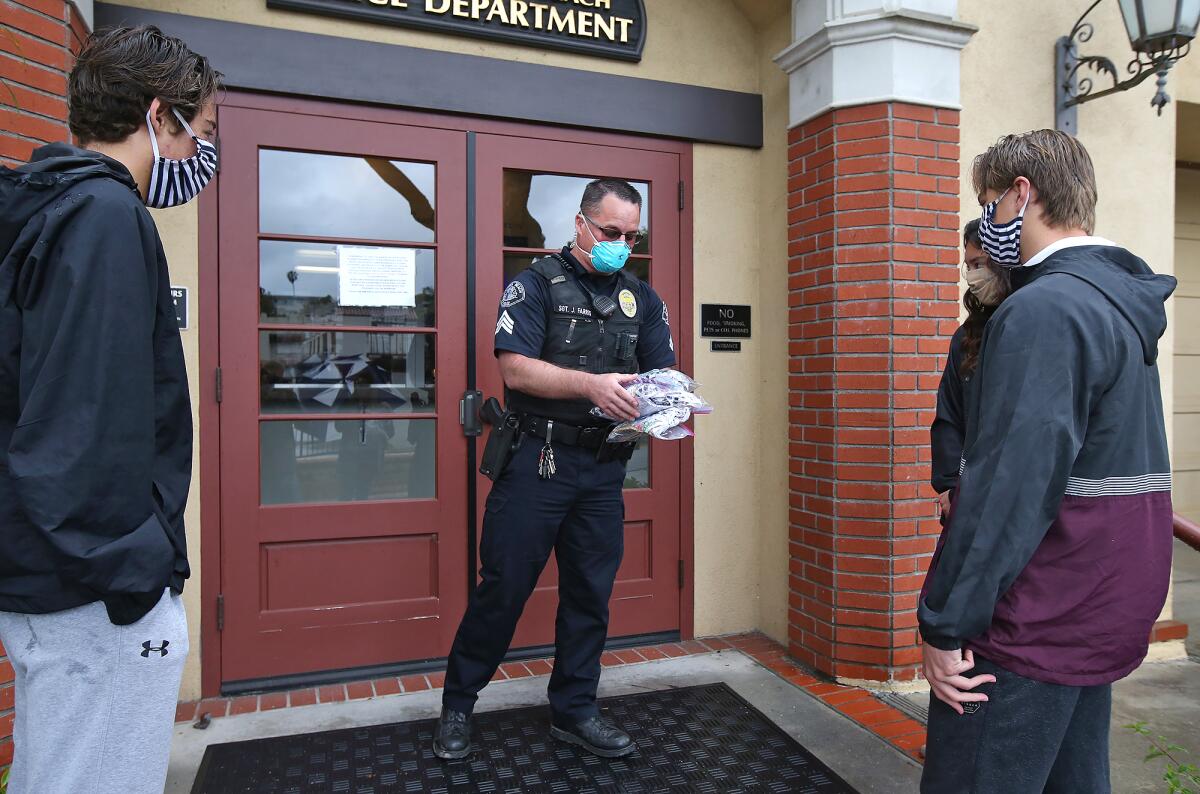 Student-athletes Michael Pinto, Jackson Golden, and Myha Pinto, donate a package of cotton masks to Sgt. Jason Farris of the Laguna Beach Police Department, center, during their donation rounds on Thursday.