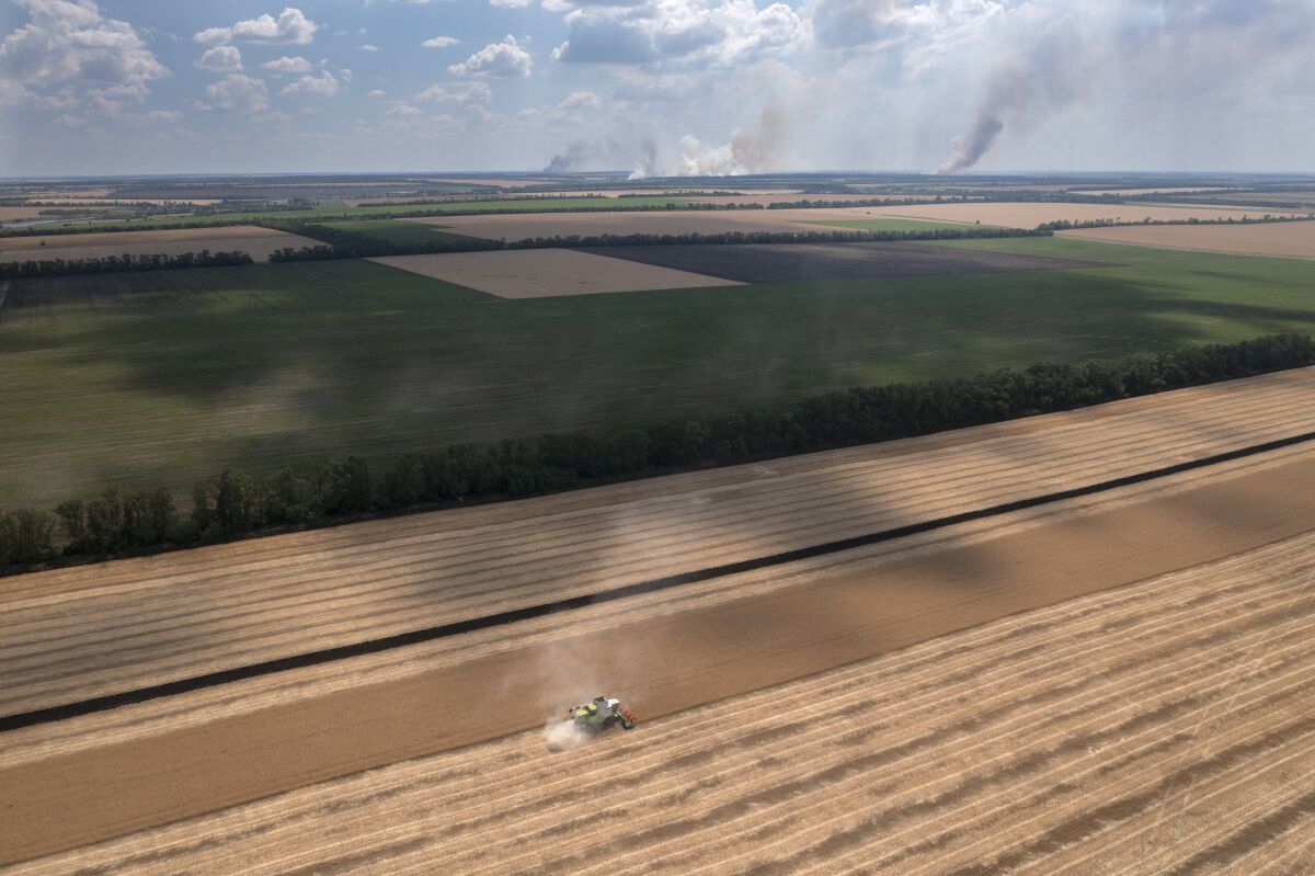 Smoke rises in the background as a farmer collects harvest in a field in the Dnipropetrovsk region, Ukraine.