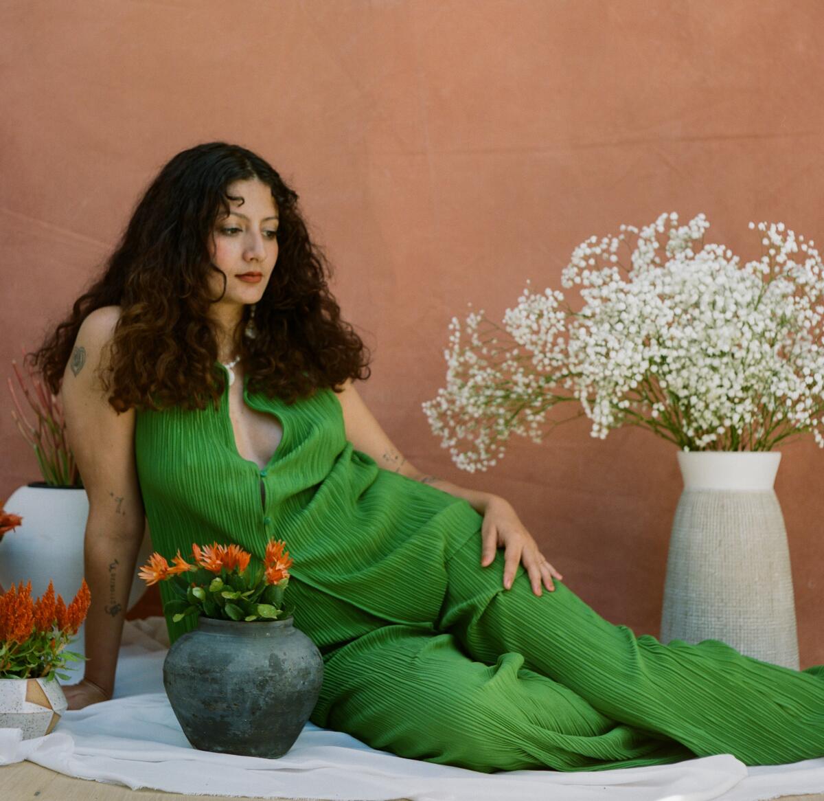 A women in a green outfit lounges between potted plants. 