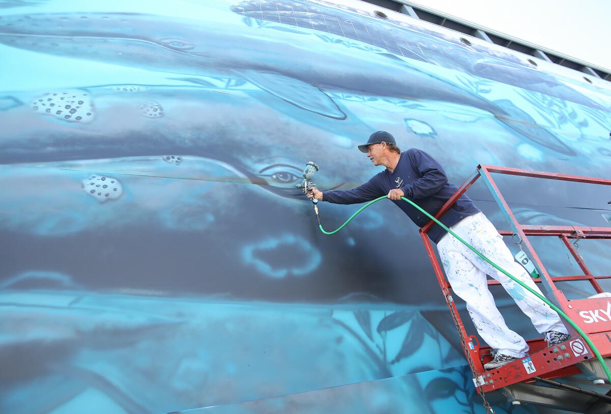 Artist Wyland adds a touch of airbrush to a whale's eye Friday as he re-creates his original "whaling wall" mural on canvas at the spot of the first one, which he painted in Laguna Beach in 1981.