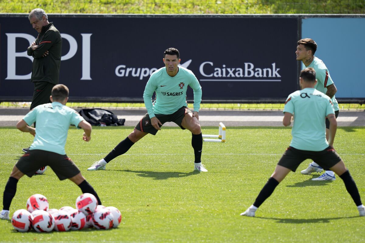Portugal's Cristiano Ronaldo, center, stretches, as Portugal coach Fernando Santos walks in the background, during a training session of the Portuguese soccer team in Oeiras, outside Lisbon, Wednesday, June 8, 2022. Portugal will face the Czech Republic June 9 in a Nations League match in Lisbon. (AP Photo/Armando Franca)