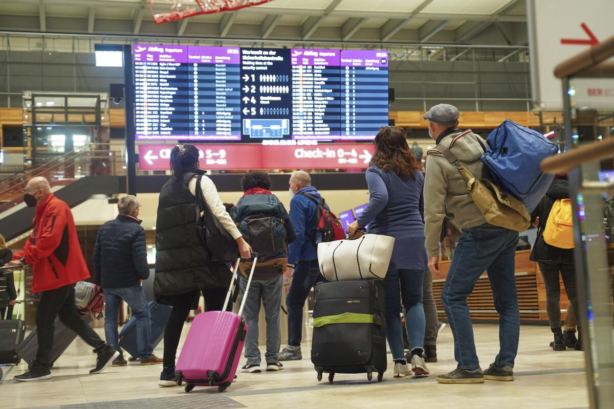 Travelers stand in front of an information board at the airport