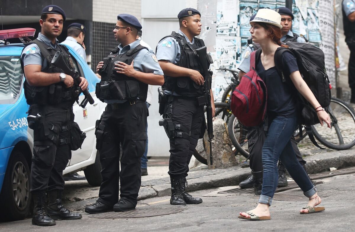 A tourist walks by as police keep watch near the Pavao-Pavaozinho neighborhood of Rio de Janiero, where violence broke out after the body of a dancer on a popular Brazilian TV show was found. Some residents claim he was tortured to death by police.