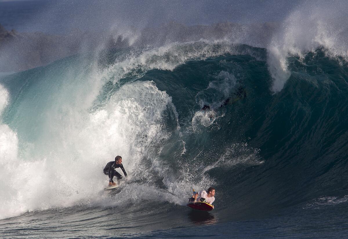 A surfer and boogie boarder ride a 10 to 15 foot wave at The Wedge in Newport Beach on Tuesday.