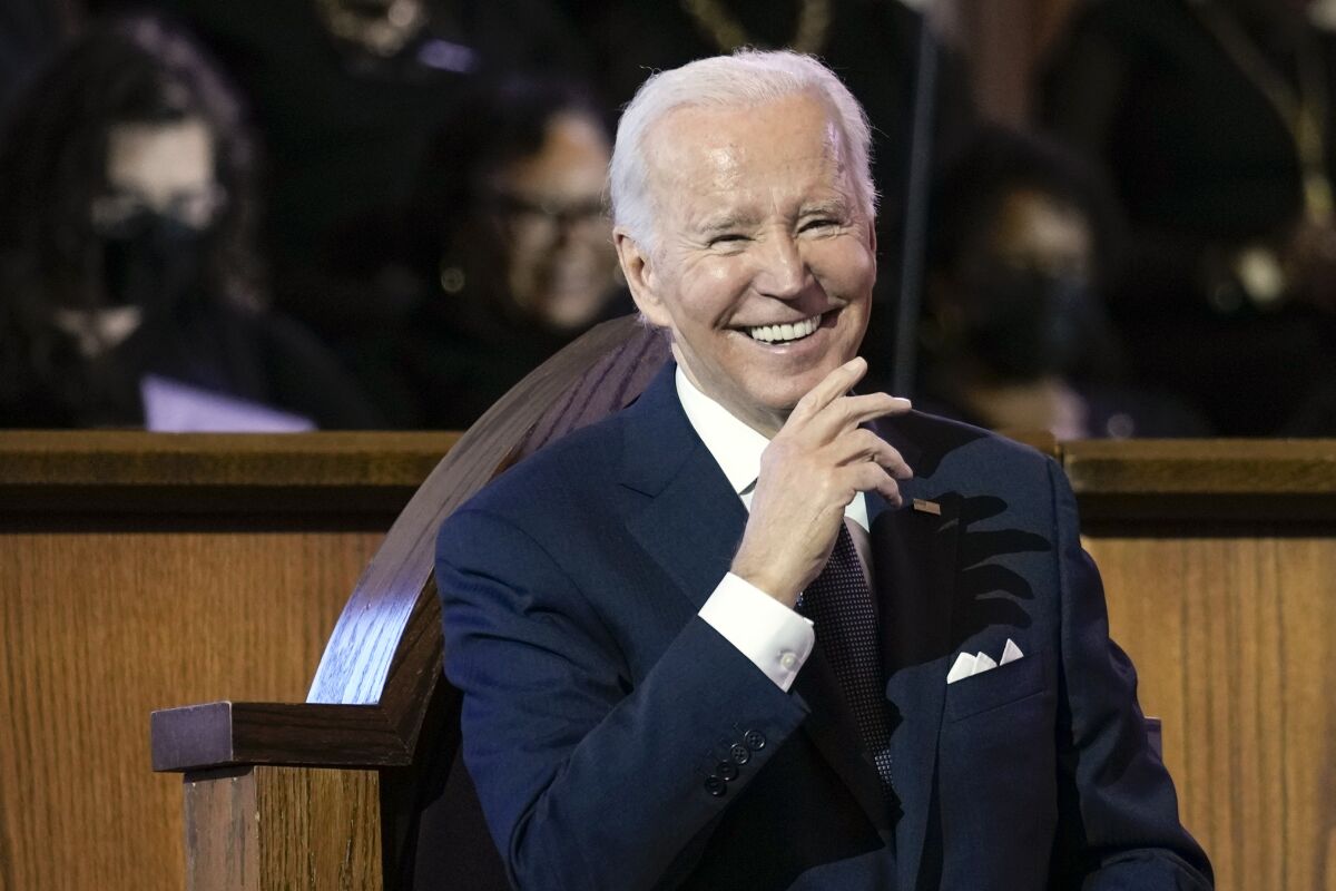 President Biden is seen sitting at a church, dressed in a dark blue suit, a white shirt and a matching pocket square