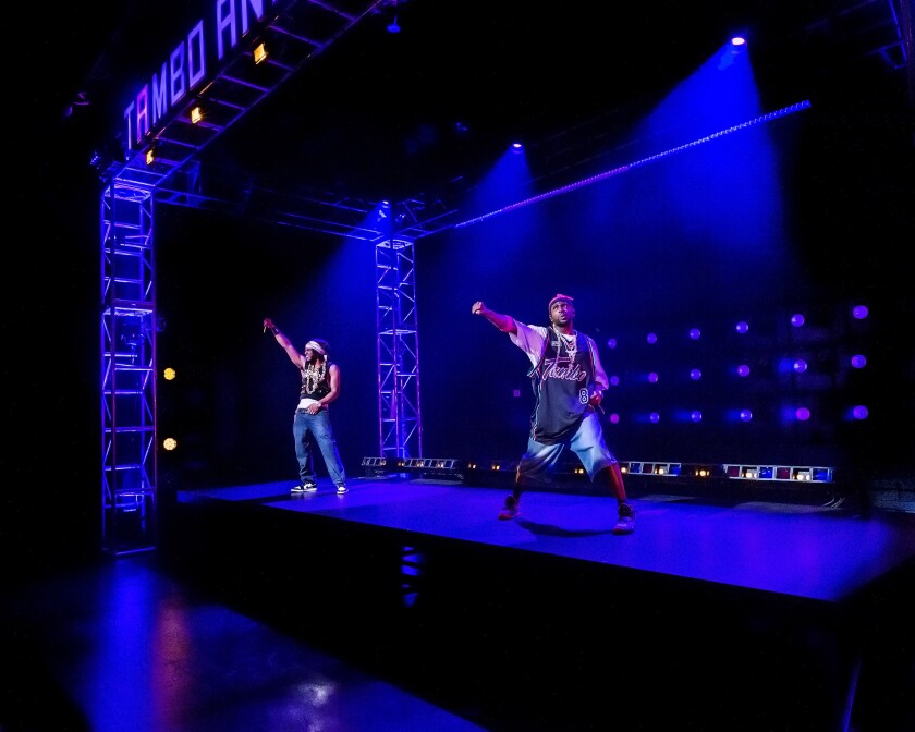 Two men strike a pose on an otherwise empty stage, each holding one fist in the air.