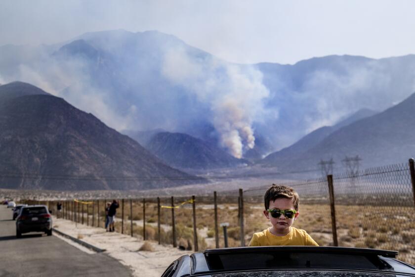 WHITEWATER, CA - SEPTEMBER 18, 2020: Elias Lomeli of Desert Hot Springs watches firefighting helicopters refill with water from his car's sunroof as the Snow fire burns in the background off Interstate 10 on September 18, 2020 in Whitewater, California. The fire is 8 miles northwest of Palm Springs and has burned more than 2,500 acres. (Gina Ferazzi / Los Angeles Times)