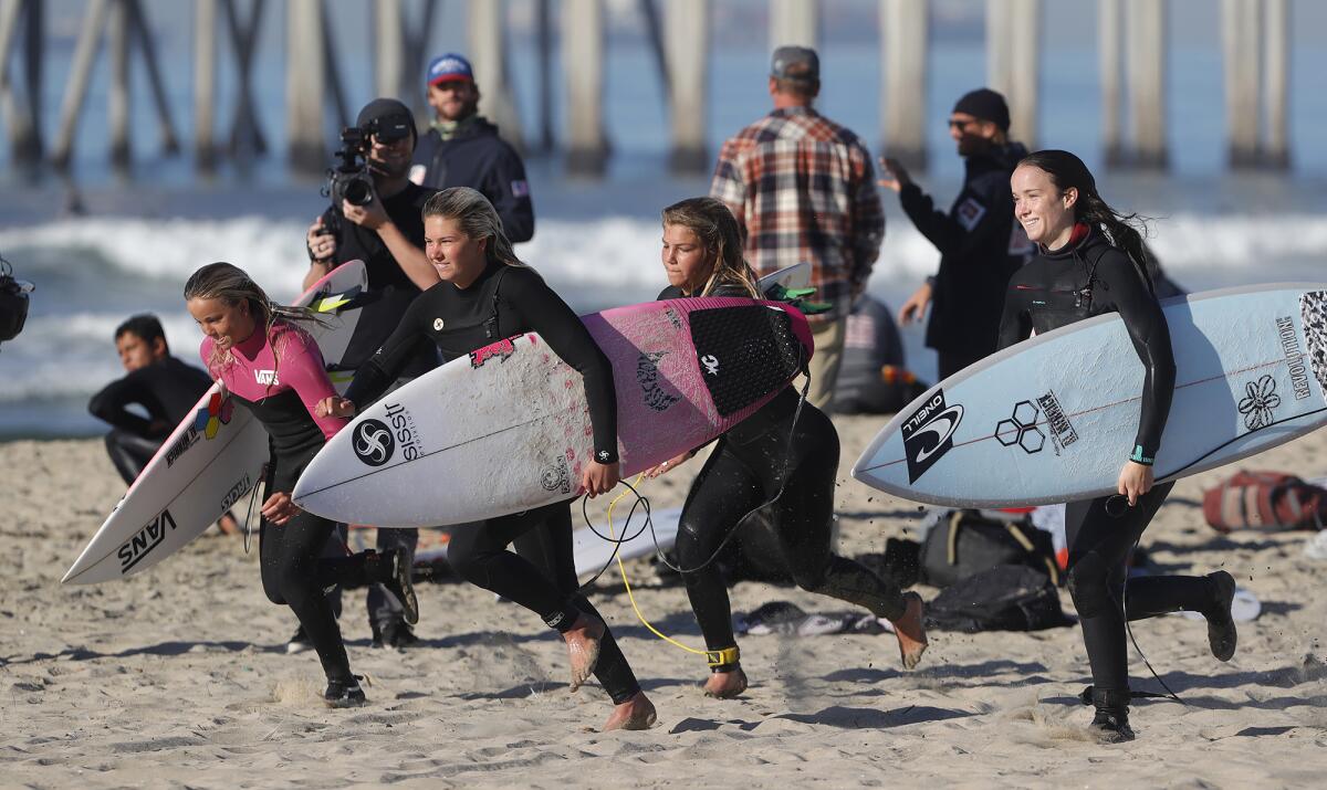 Members of the girls' USA Surfing junior team sprint up the beach.