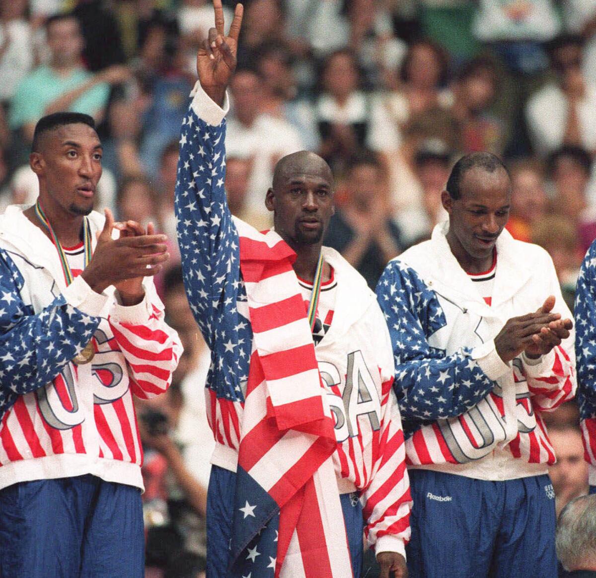 The United States' Michael Jordan, center, poses Aug. 8, 1992, with his gold medal during the Barcelona Olympics with a flag dropped over his shoulder to hide a rival sponsor's logo on his jacket.