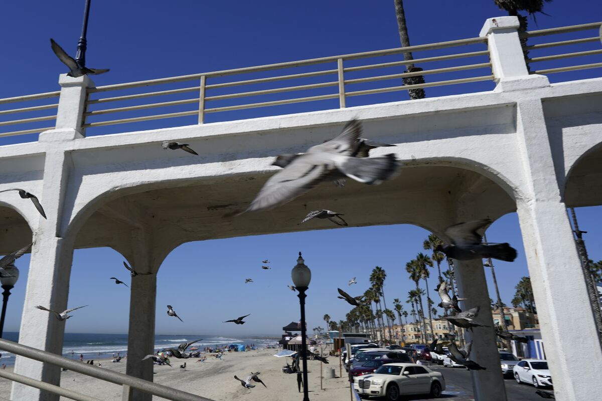 Birds fly past a bridge connecting the Oceanside pier to Pacific Street Friday, Oct. 15, 2021, in Oceanside, Calif. The iconic bridge is deteriorating because the city lacks the money for a roughly $25 million rehabilitation. One reason the project has slowed while projects in other cities are moving ahead revolves around the American Rescue Plan — the sweeping COVID-19 relief law championed by President Joe Biden and congressional Democrats that is pumping billions of dollars to states and local governments. (AP Photo/Gregory Bull)