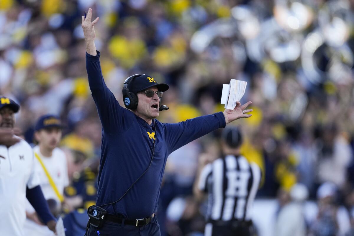 Michigan coach Jim Harbaugh raises his arms overhead along the sideline during a game.