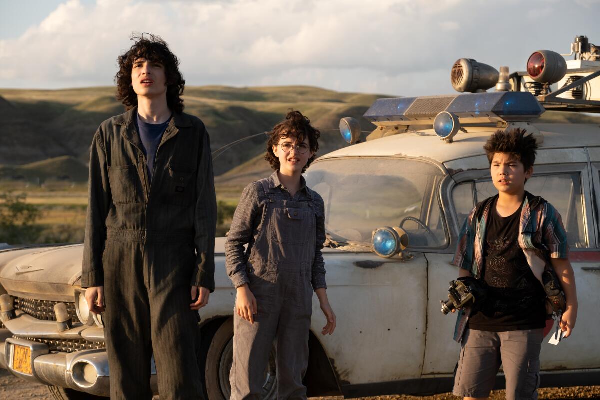 Three kids stand in front of a converted ambulance in the movie "Ghostbusters: Afterlife."