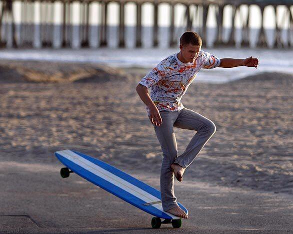 Anders Hamborg, 18, hangs five while crossing his legs, a move that complements his surfing style, on a 6-foot 8-inch long Hamboard skateboard along the Huntington Beach bike path.