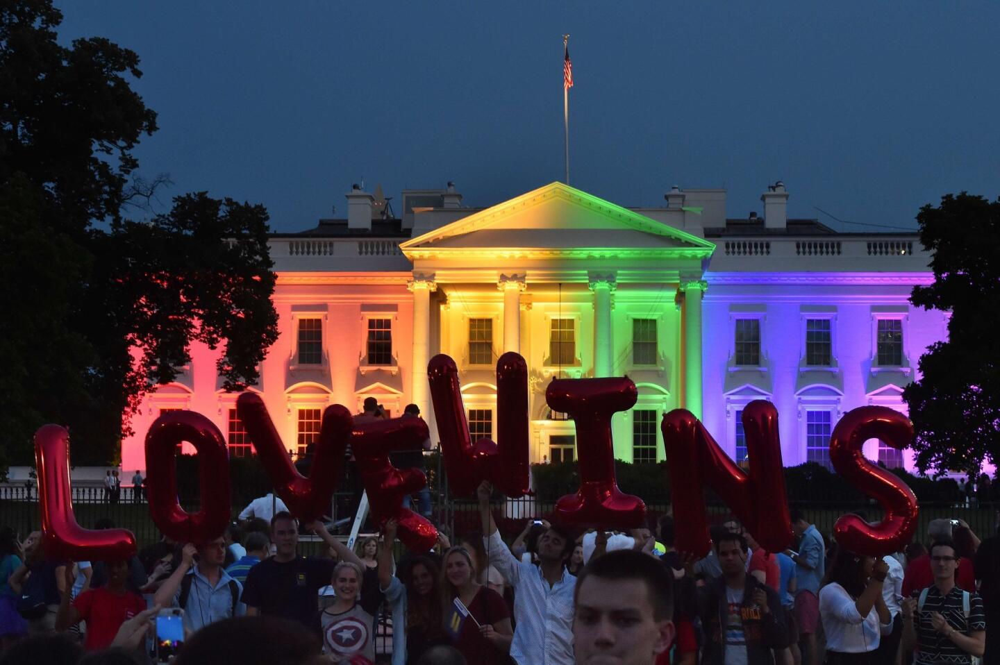 People hold balloon letters reading, "Love wins," on June 26, 2015, in front of the White House illuminated by rainbow colors in Washington.