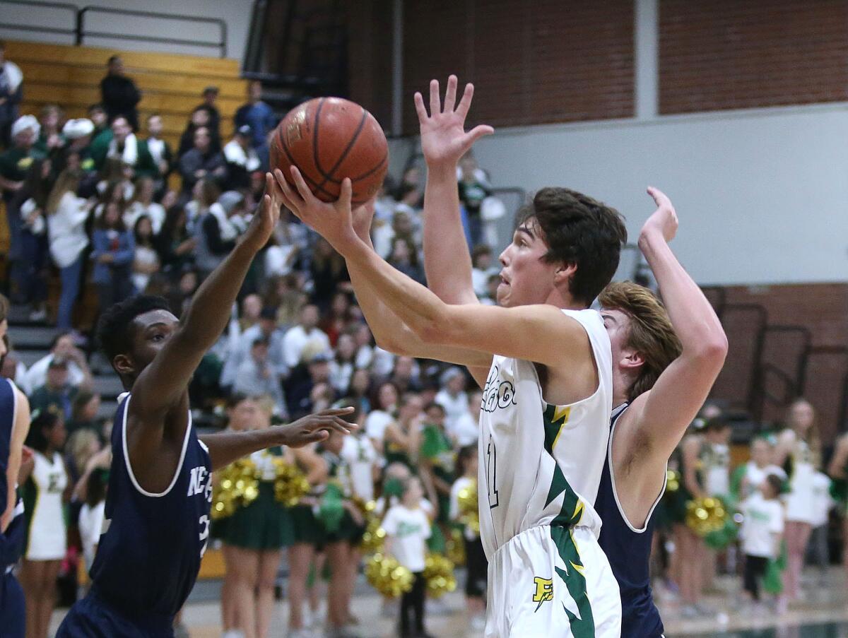 Edison’s Bradley Luna drives in for a layup while being defended by Newport Harbor’s Josh Sandy, left, and Robbie Spooner, right, during a Surf League game on Friday.