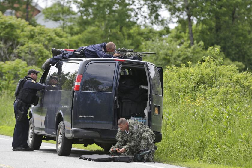 A law enforcement agent looks through a sniper scope while another in camouflage assembles a weapon during a search for two escaped killers in Boquet, N.Y., on Tuesday.