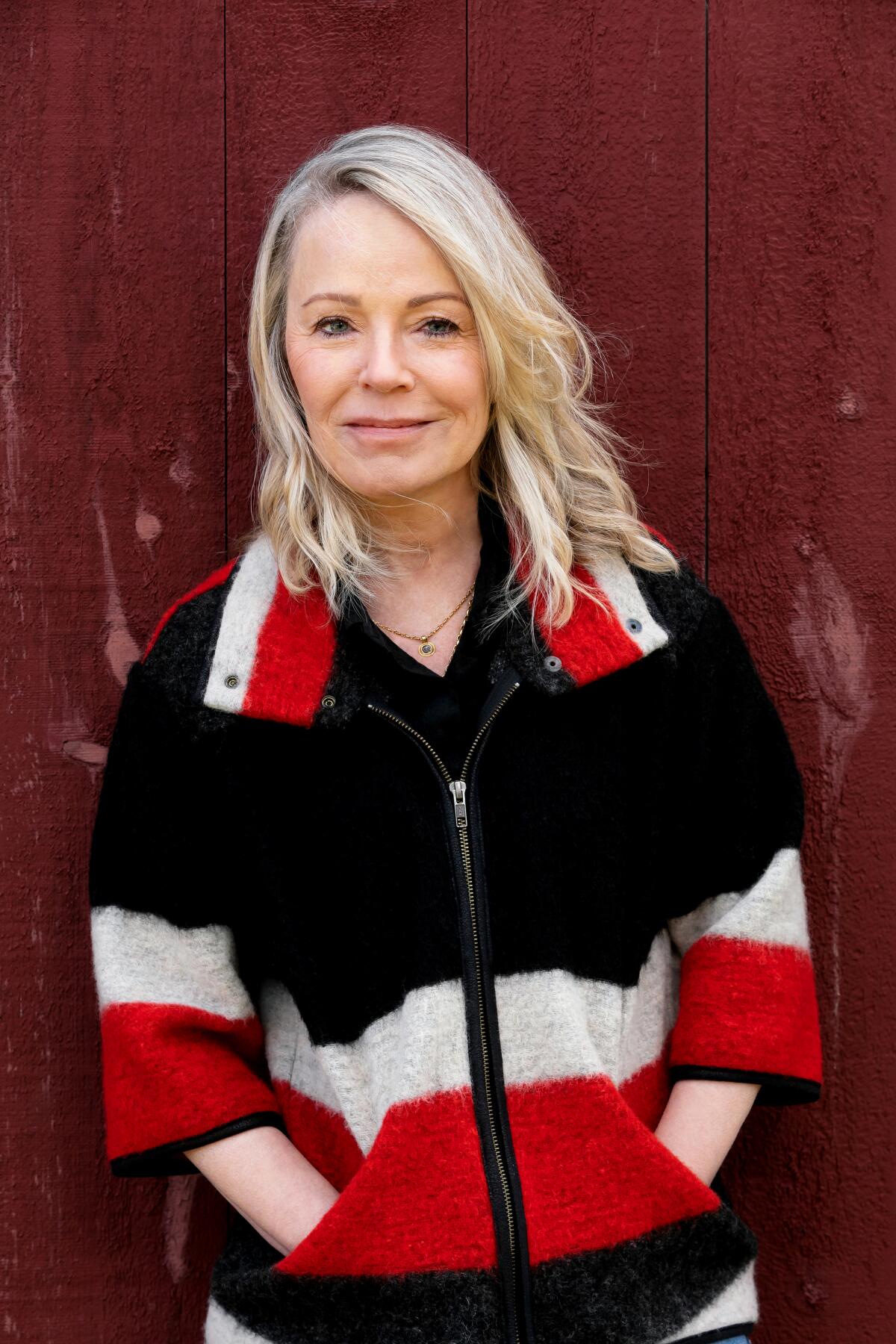A woman with blonde hair wears a dark fleece jacket with wide red and white stripes.