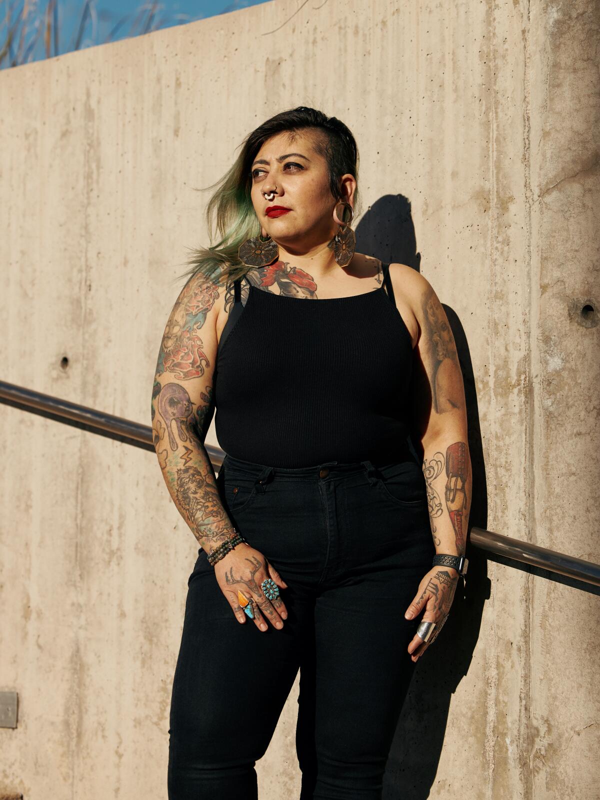 woman in a black tank and black pants outside by a concrete wall 