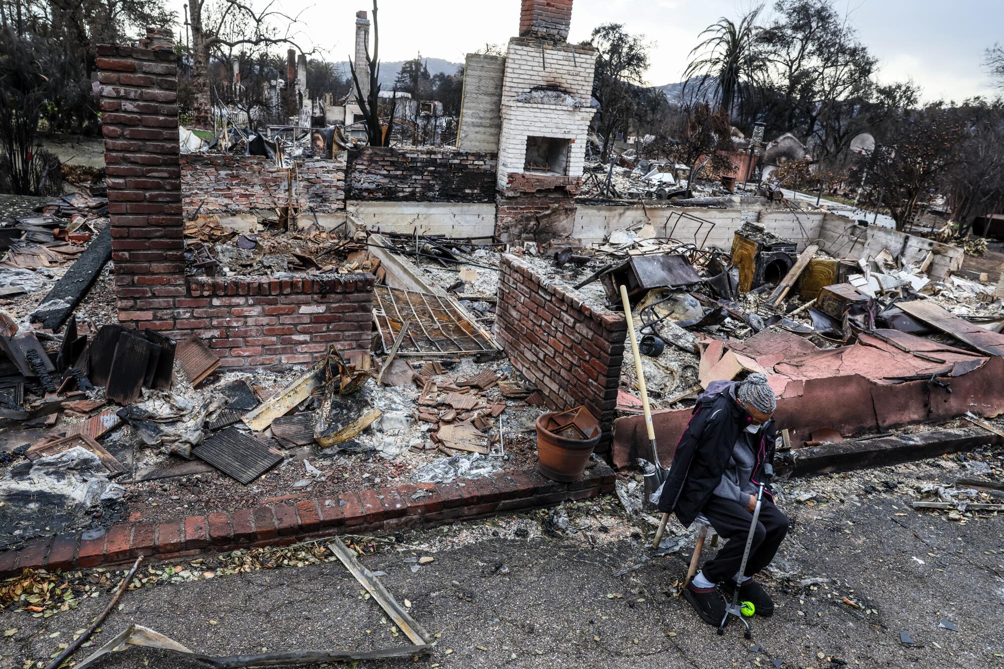 A woman sits before the ruins of a home destroyed in a fire.