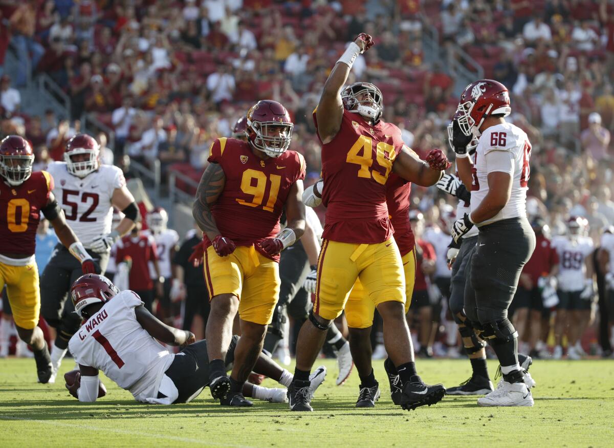 USC defensive linemen Tuli Tuipulotu raises an arm near other USC players and a Washington State player on the ground.