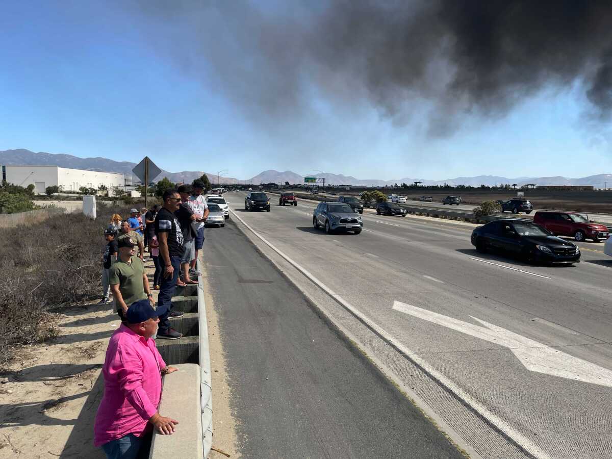 People stand on the side of a road looking at black smoke