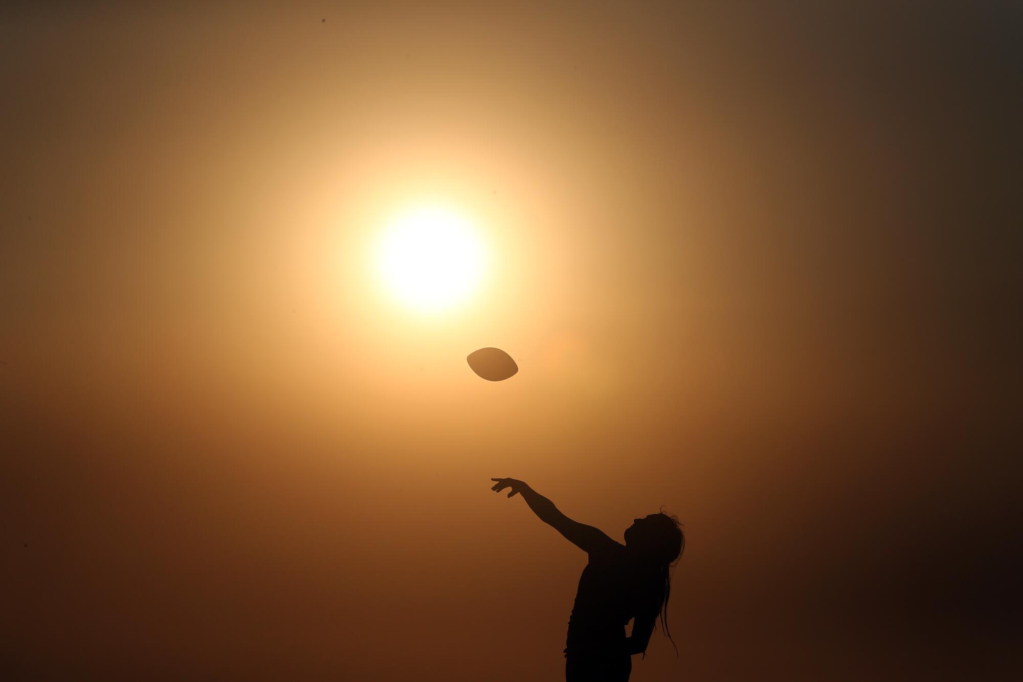 Silhouette of a person throwing a football in front of a yellow sun at the beach