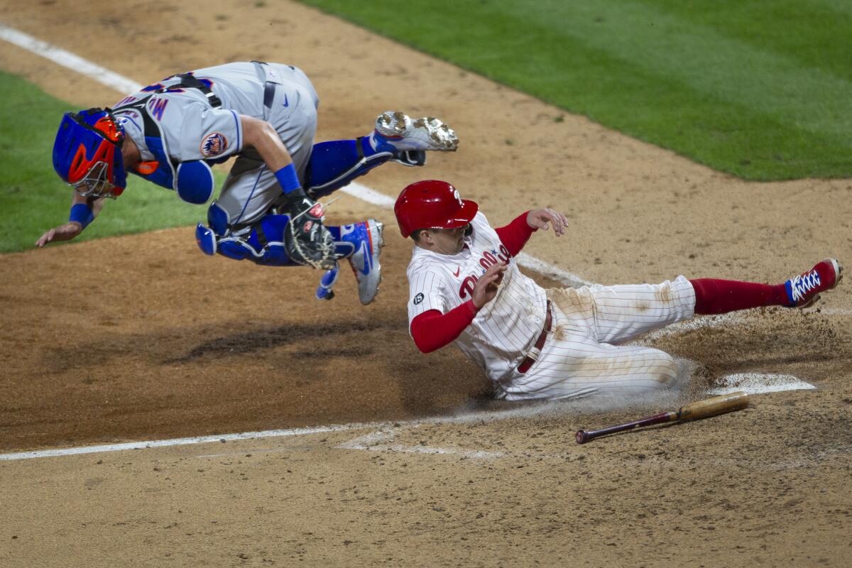 Philadelphia Phillies first baseman Rhys Hoskins (17) scores on an RBI single as New York Mets catcher James McCann (33) goes airborne before he can make the tag during the eighth inning of a baseball game, Monday, April 5, 2021, in Philadelphia. (AP Photo/Laurence Kesterson)