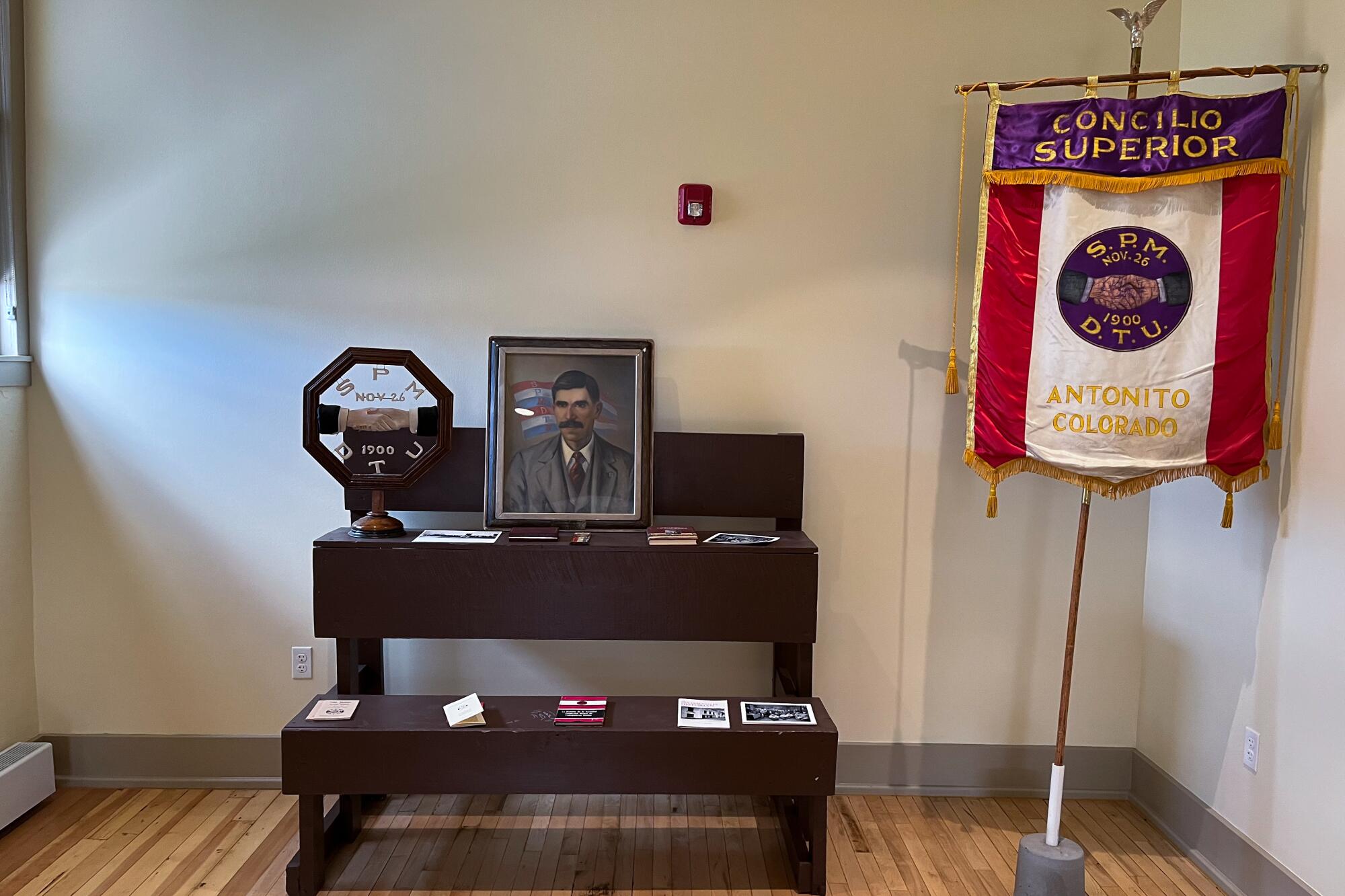 A brown wooden altar bearing a portrait of a man and other items, next to a red, white and purple banner on a stand