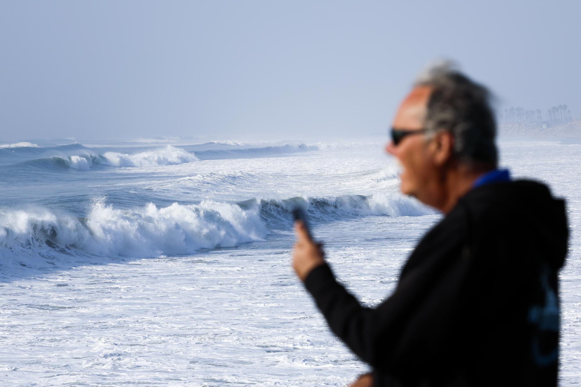 A man captures the large surf on his phone from the Huntington Beach Pier as a powerful swell reaches Southern California.
