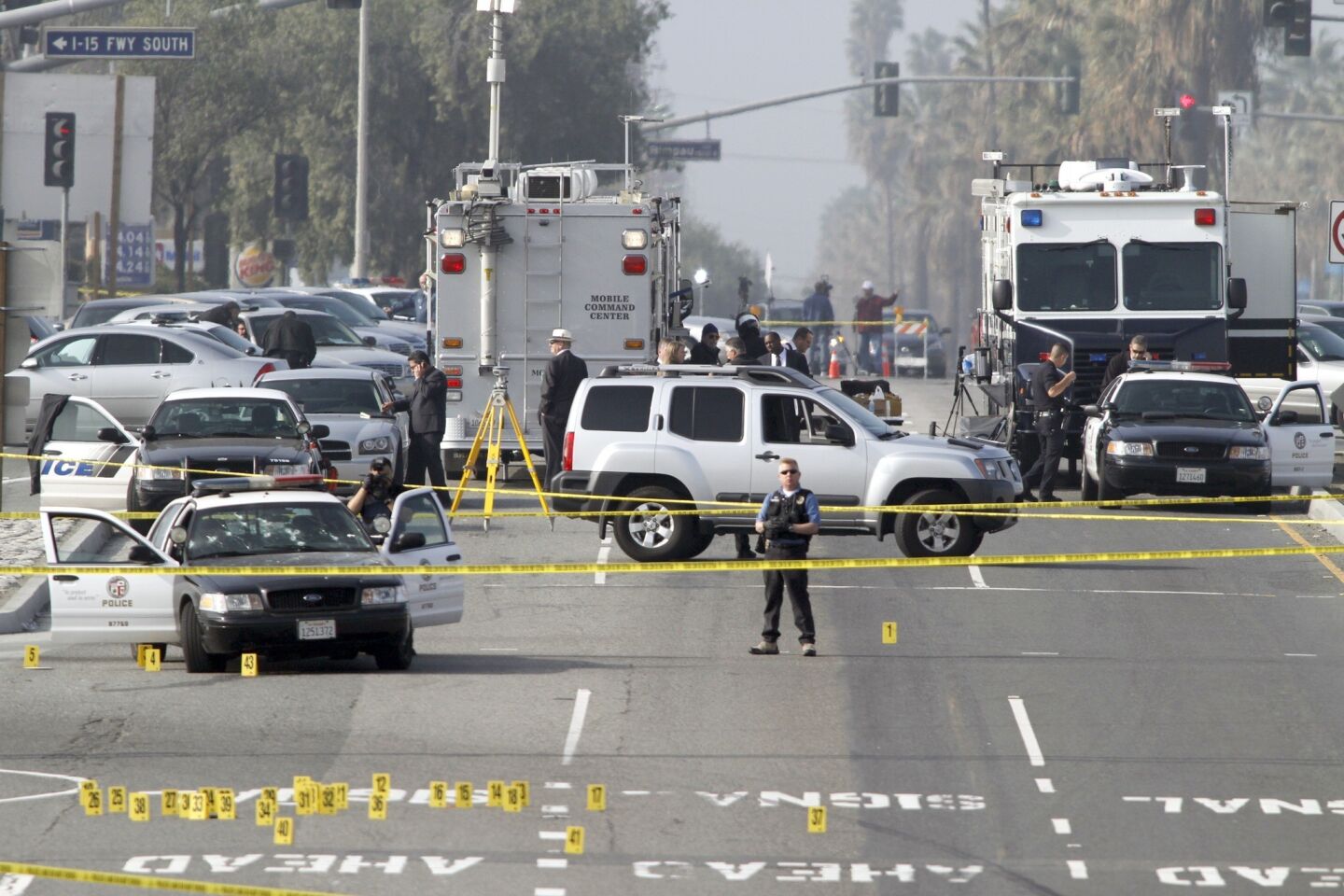 Police investagators look at the LAPD car, left , where an officer was wounded on Magnolia Avenue in Corona