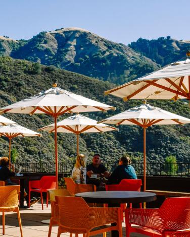 A collection of shaded patio tables near the green coastal mountains of Big Sur.