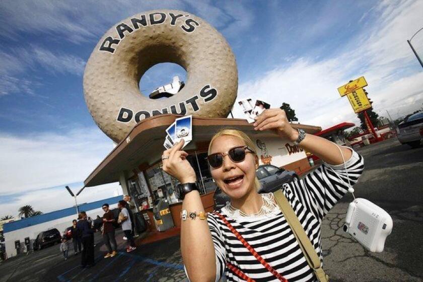 Tourist Mika Shima, 26, of Tokyo holds up photos she took of Randy's Donuts.