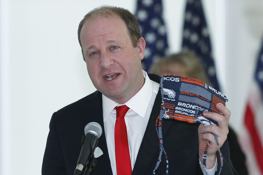 Colorado Gov. Jared Polis holds up his face mask on Sunday as he explains guidelines for the state's reopening.
