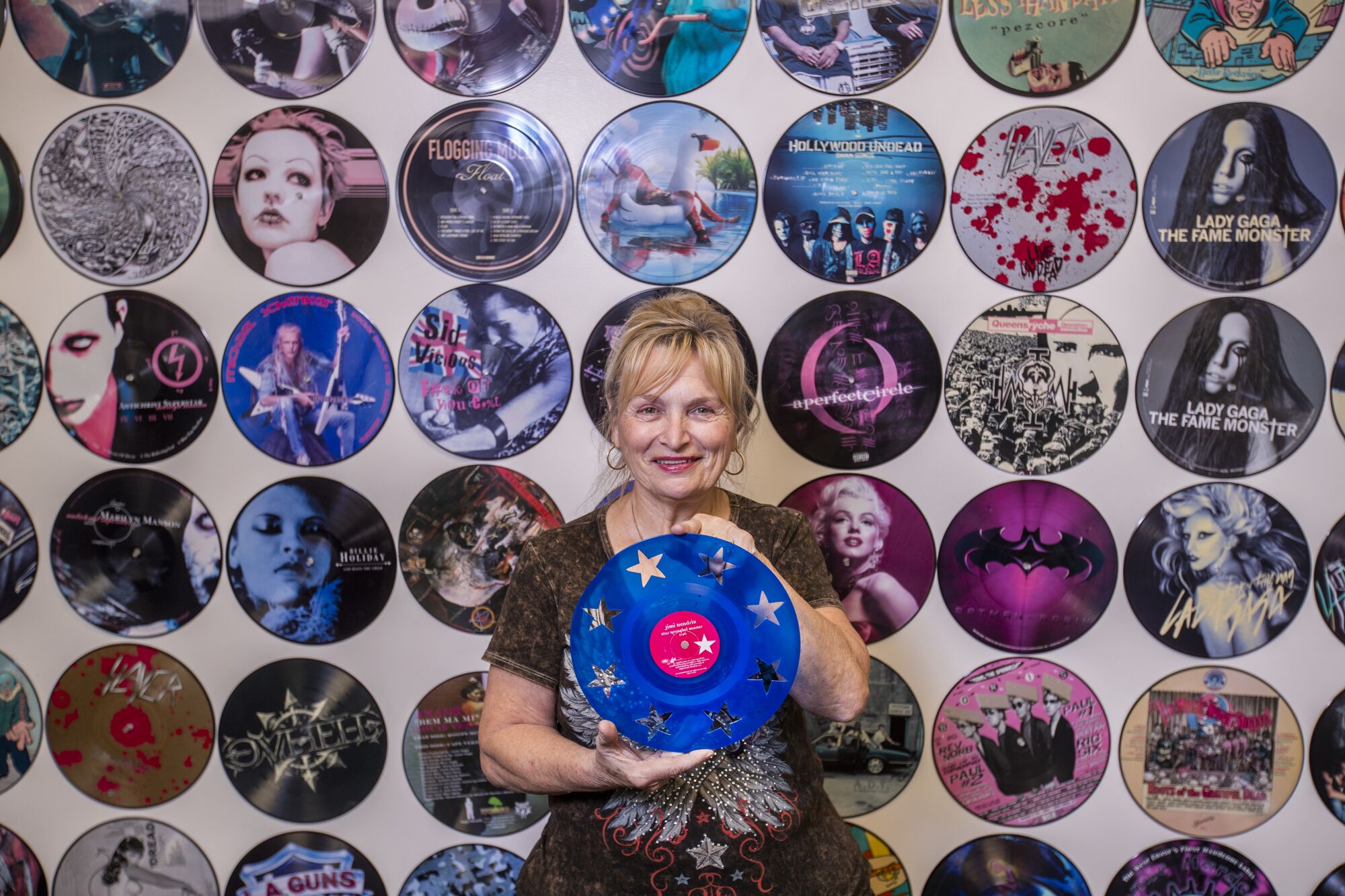 A woman holding a blue vinyl LP, in front of a wall of picture disc albums.