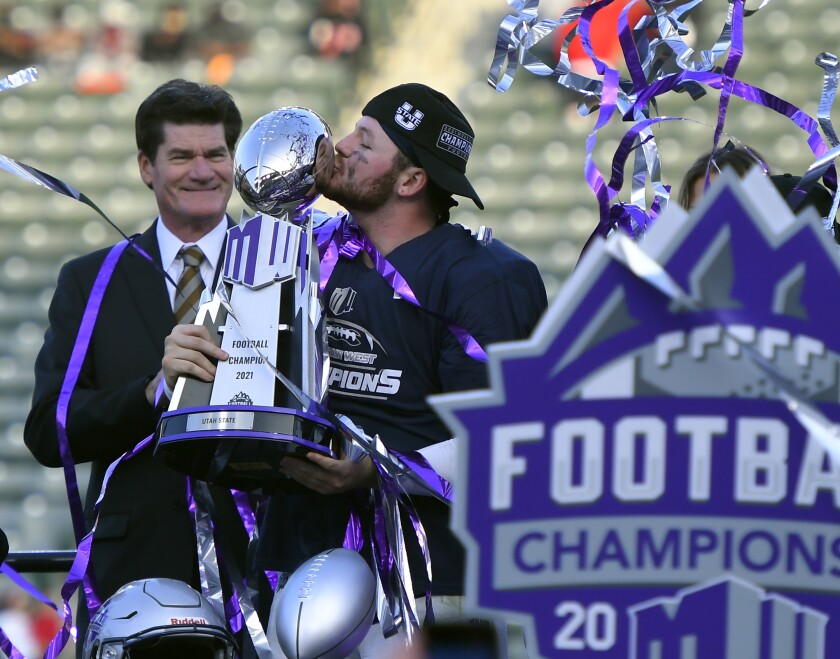 Craig Thompson, Mountain West Conference commissioner, stands next to Utah State quarterback Logan Bonner (1) who kisses the trophy after defeating San Diego State during an NCAA college football game for the Mountain West Conference Championship, Saturday, Dec. 4, 2021, in Carson, Calif. (AP Photo/John McCoy)