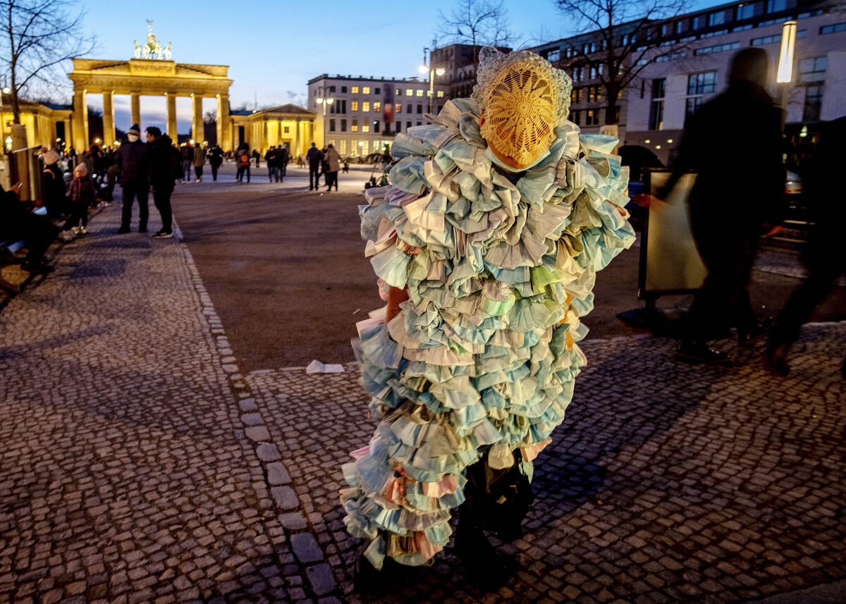 File---File picture shows a woman wearing a dress made of hundreds of face masks as she comes back from an anti corona demonstration in Berlin, Germany, Saturday, Feb. 12, 2022. In background is the Brandenburg Gate. (AP Photo/Michael Probst,file)