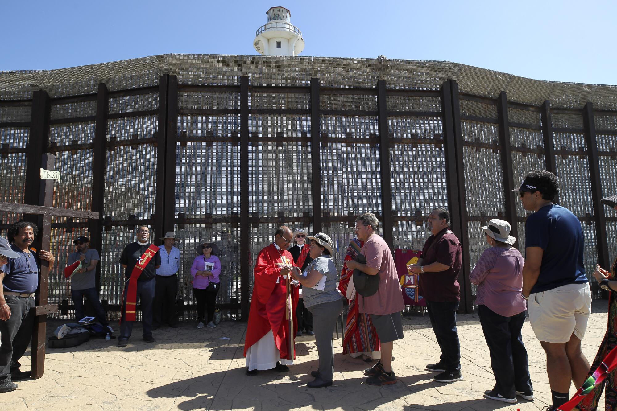 People line up near the border wall to take Communion.